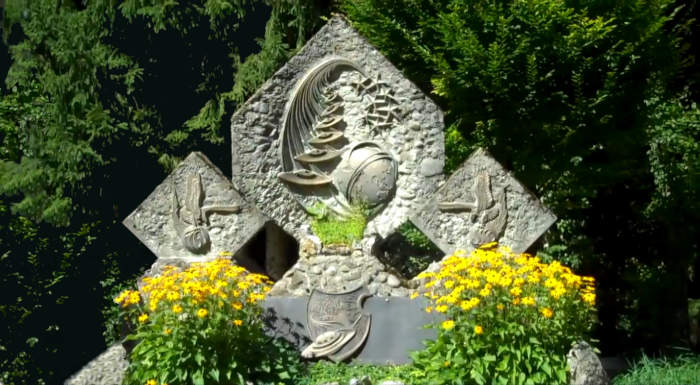 Monumento in pietra composto in 3 parti, e 2 piccole aiuole di fiori gialli davanti